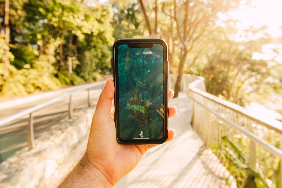A visitor holding a phone on an outdoor boardwalk with Future Nature AR content visible on screen.